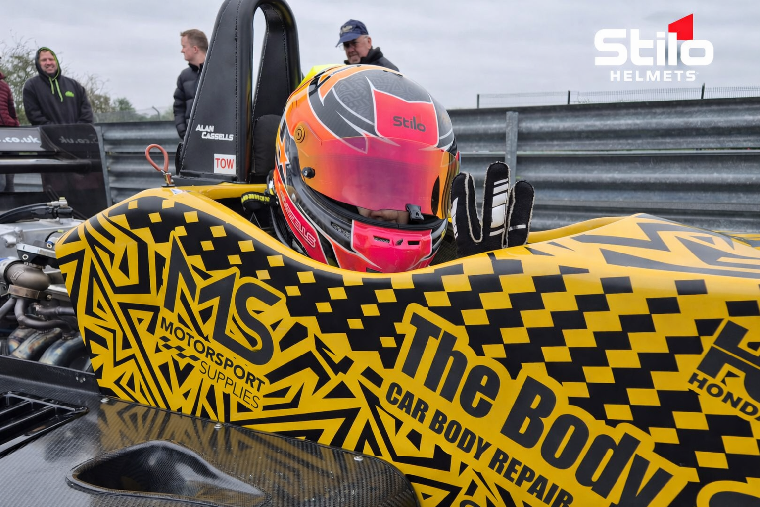 Person wearing a racing helmet inside a car with 'Stilo Helmets' branding.